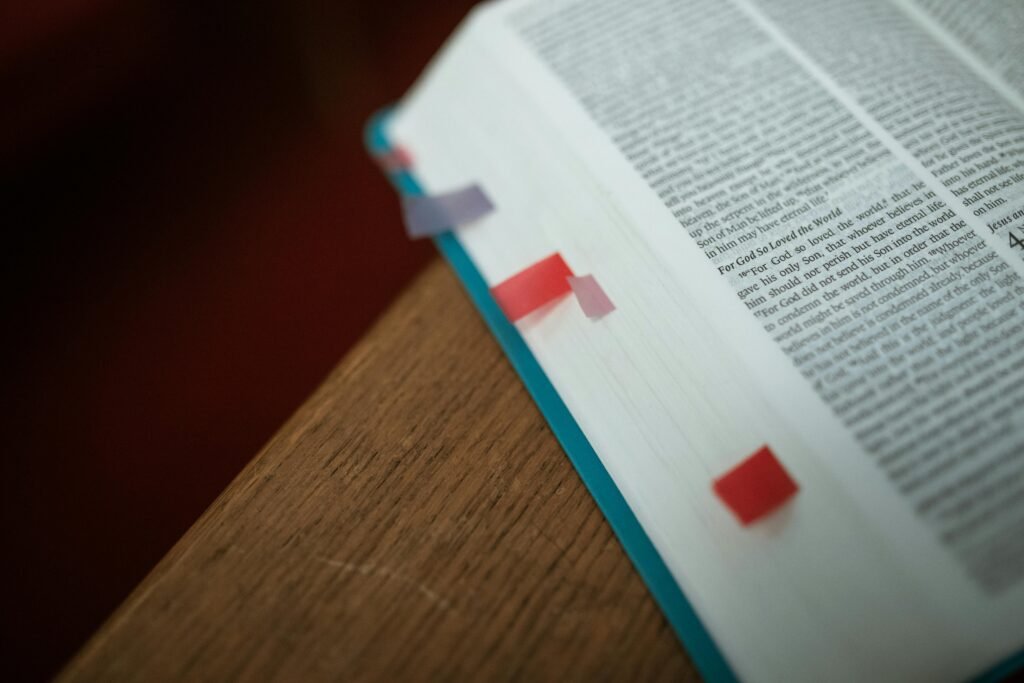 Close-up of an open Bible with colorful bookmarks on a wooden desk.