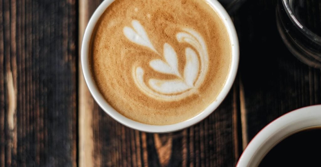 A beautifully crafted cappuccino with latte art surrounded by coffee cups on a rustic wooden table.