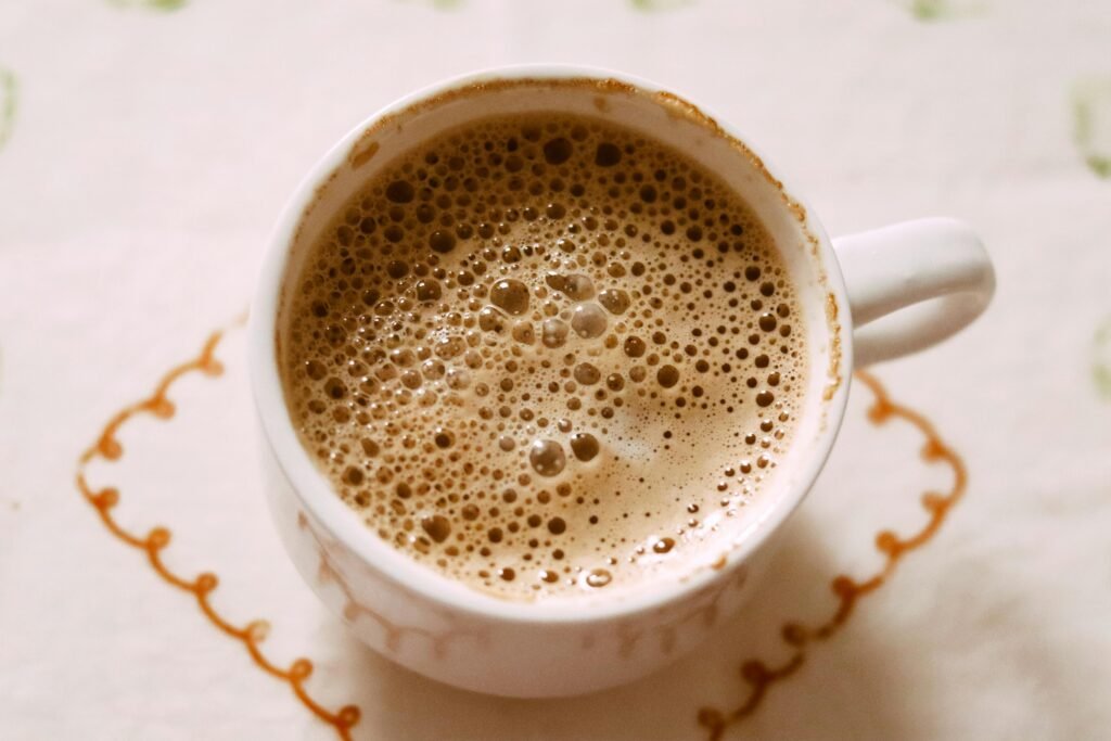Top view of a creamy foamy coffee in a white ceramic cup on a patterned tablecloth.