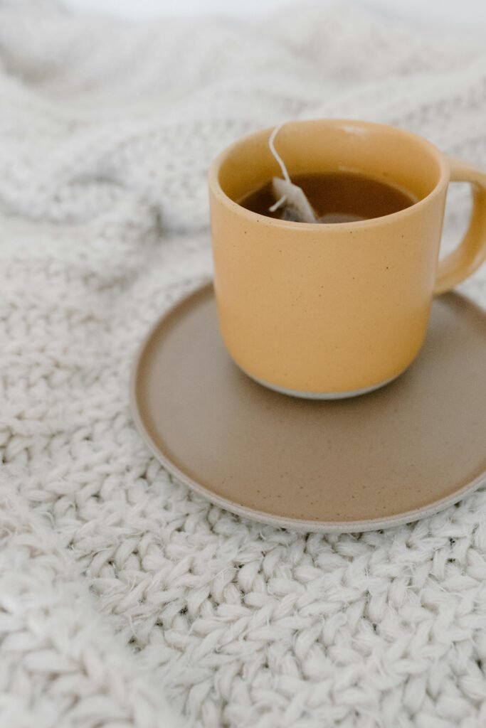 Warm tea cup on a textured white knitted blanket, evoking cozy, minimalist vibes.