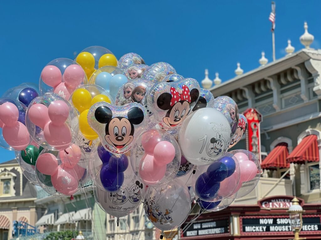 A Dream is a Wish Your Heart Makes Vibrant Disney character balloons in front of theme park cinema under blue sky.