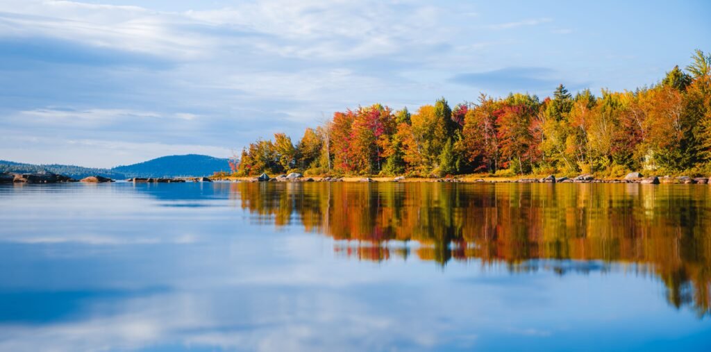 Vibrant fall foliage reflecting on Tunk Lake, Steuben, Maine, offering a serene autumn landscape.
